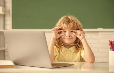 Gülümseyen gözlüklü çocuk okulda bilgisayar ve okulla çevrimiçi ders çalışıyor.