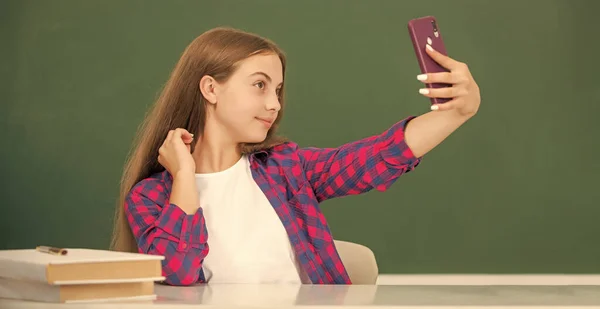 Bambino sorridente a scuola facendo selfie sul telefono su sfondo lavagna, vlog — Foto Stock