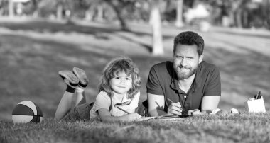 Baba ve oğul parkta çimenlerde rahatlar çizim yapmayı öğrenir, aile hafta sonu