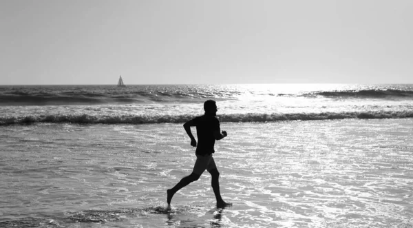 Wysportowany człowiek biegacz sylwetka biegać na letniej plaży z wodą morską i słońcem, wytrzymałość — Zdjęcie stockowe