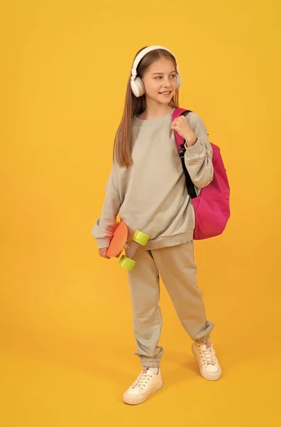 Okul çantalı ve panolu mutlu genç kız. Kulaklıkla müzik dinle, okul zamanı.. — Stok fotoğraf