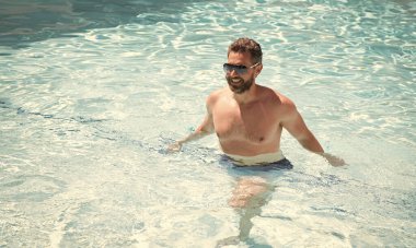 Yaz tatilinde havuzda yüzen güneş gözlüklü mutlu sakallı adam.