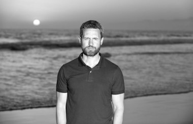 Yaz tişörtlü sakallı yakışıklı adam sahilde gün batımlı, yaz tatilinde.