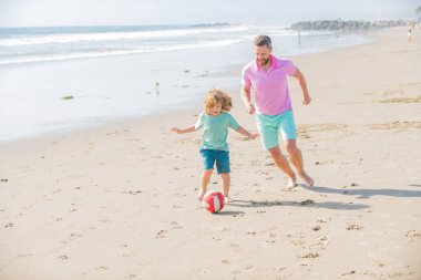 Mutlu baba ve oğul yaz kumsalında top ve arkadaşlıkla futbol oynuyorlar.