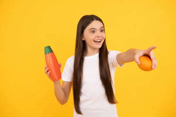 Menina feliz segurar grapefruit shampoo apontando dedo. apresentando produto cosmético para adolescente — Fotografia de Stock