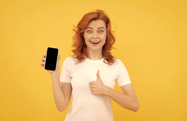 Eccitato giovane donna isolato sfondo giallo con il telefono cellulare mostrando gesto ok. — Foto Stock