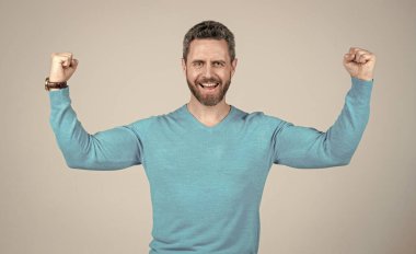 Sakallı mutlu olgun bir adam gri arka planda güç ve güç gösteriyor.