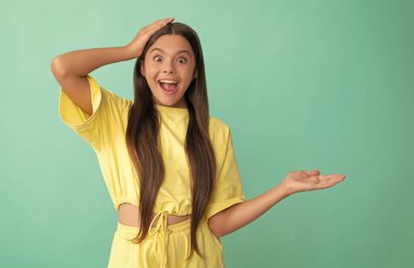 Şaşırmış genç kız, ürünü mavi arka planda fotokopi alanı ile sunuyor.