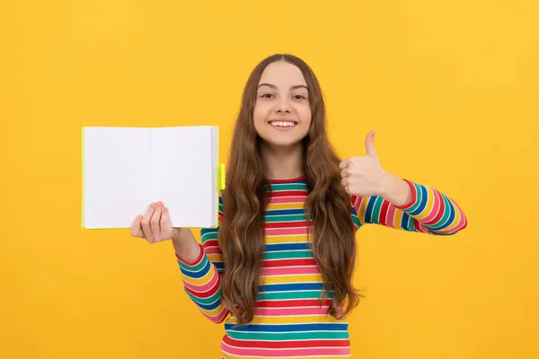 Happy kid geven duimen omhoog hand gebaar houden open boek voor kopieerruimte gele achtergrond, tevreden — Stockfoto