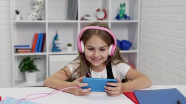 Kulaklıklı mutlu çocuk sınıfta cep telefonuyla video izliyor, video görüşmesi yapıyor.