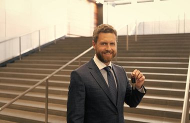 Gayrimenkul. Takım elbiseli mutlu adam arabanın anahtarlarını tutuyor. Olgun başarılı iş adamı ev anahtarıyla