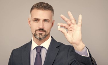 Gri saçlı, takım elbiseli olgun iş adamı elinde hapla tamam jest yap, enerji tedavisi yap.