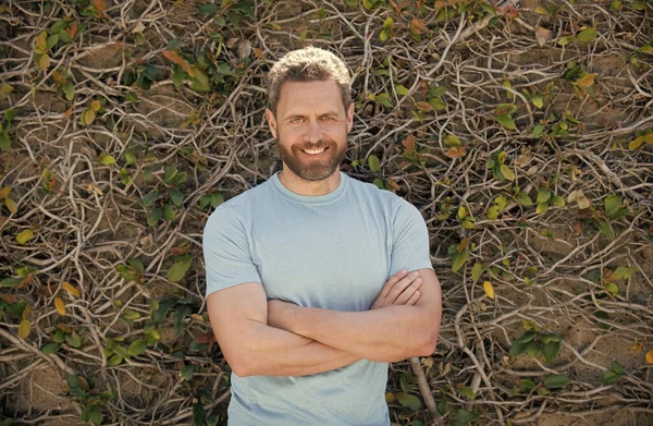 Счастливый бородатый взрослый мужчина в летней рубашке на фоне стены растения, летний стиль — стоковое фото