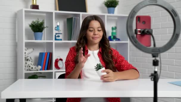 Teen girl presenting cactus plant in front of smartphone selfie lamp, vlogging — Stock Video