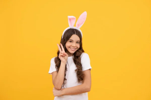 Niño alegre en orejas de conejo sobre fondo amarillo mostrar la paz, Pascua —  Fotos de Stock