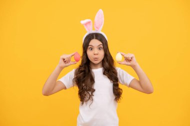 Tavşan kulaklı neşeli çocuk sarı arka planda yumurtaları tutuyor, mutlu Paskalyalar.