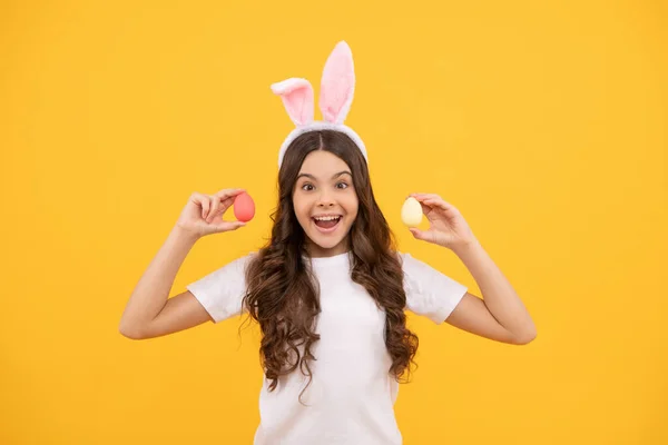 Zdumione dziecko w uszach króliczka trzymać jaja na żółtym tle, szczęśliwy Wielkanoc — Zdjęcie stockowe