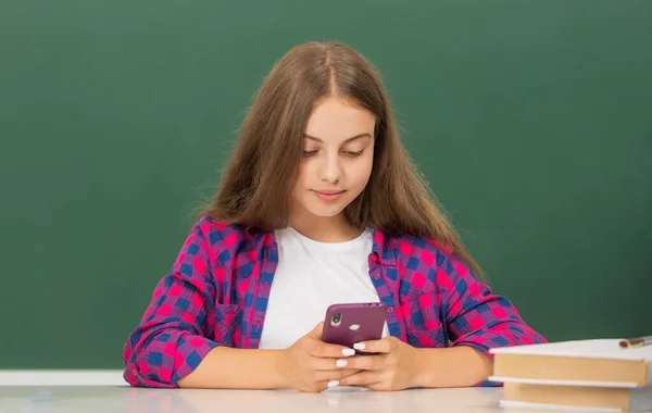 Upptagen tonåring flicka skriva meddelande på mobiltelefon i gymnasiet på svarta tavlan, meddelande — Stockfoto