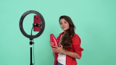 Güzel çocuk için şampuan reklamı. Uzun dalgalı saçlarını sallıyor. Lamba ve vlogla blog yapıyor.