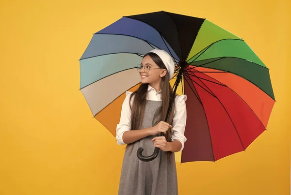 Fröhliches Teenie-Mädchen in Baskenmütze unter buntem Regenschirm zum Regenschutz in der Herbstsaison, Kindheit. — Stockfoto