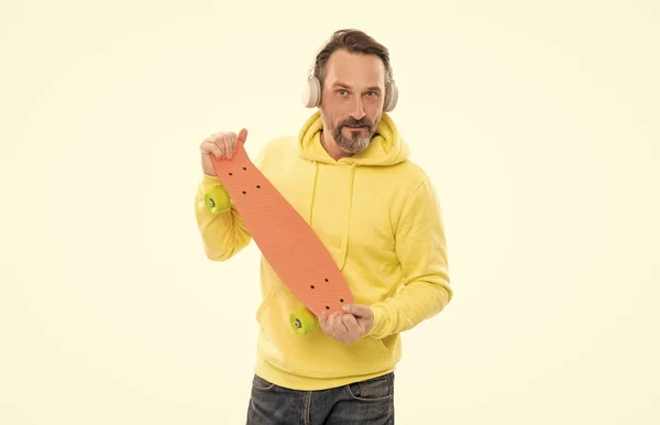 Šťastný muž poslouchat hudbu ve sluchátkách držet penny skateboard izolované na bílém, skateboard kultury. — Stock fotografie