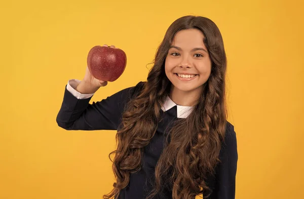 Щаслива дівчина-підліток, що показує червоне вітамінне яблуко на обід на жовтому фоні, вітамін — стокове фото