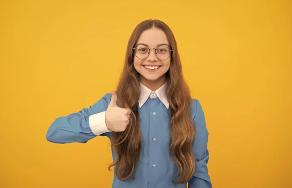 Happy nerdy-vypadající dívka dítě dát palce nahoru spokojenost ruka gesto žluté pozadí, dětství — Stock fotografie
