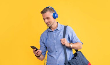 Gülümseyen adam dinle. Akıllı telefondan sohbet et. Sarı arka planda seyahat çantasıyla sohbet et..