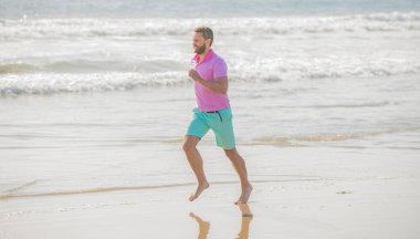 Yaz plajında koşan olgun atletik adam eğitim ve başarı için koşuyor.