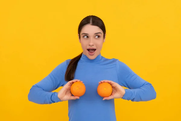 Sarı arka planda turuncu turunçgil meyvesi tutan genç bir kadın. Doğal yiyecek. — Stok fotoğraf