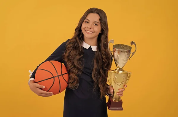 Šťastný dospívající dívka držet basketbal a šampion pohár na žlutém pozadí, šampion — Stock fotografie