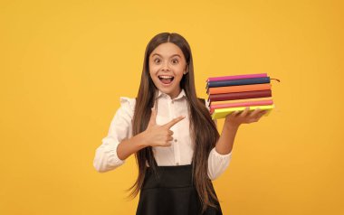 Okul üniformalı genç kız kitap yığınını işaret ediyor.