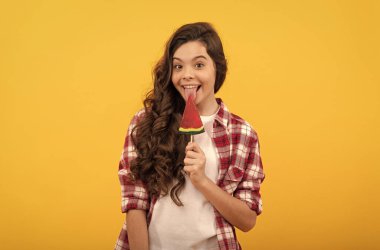 Uzun kıvırcık saçlı mutlu çocuk sarı arka planda lolipop karamel şekeri yaladı, çocukluk..