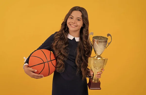 Feliz adolescente menina segurar bola de basquete e copo campeão no fundo amarelo, campeão — Fotografia de Stock
