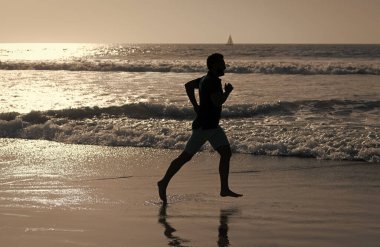 Yaz plajında deniz suyu ve güneşle koşan atletik adam silueti, motivasyon