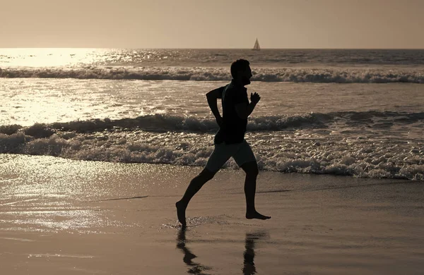 Wysportowany człowiek biegacz sylwetka biegać na letniej plaży z wodą morską i słońcem, motywacja — Zdjęcie stockowe