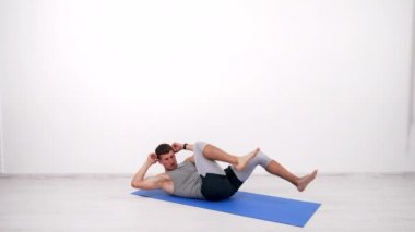 Spor yapan kaslı sporcu spor paspası üzerinde bisiklet egzersizi yapıyor.