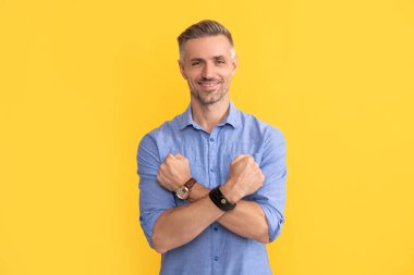 Gülümseyen adam kol saati ile kollarını kavuşturdu sarı arka planda, zaman ölçüsü