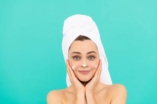 Vrolijke jonge vrouw aanbrengen gezicht crème op blauwe achtergrond — Stockfoto