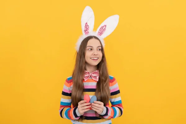 Gelukkig tiener meisje in konijn oren en strikje houden paaseieren op gele achtergrond — Stockfoto