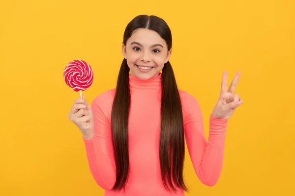 Happy child with lollipop candy on stick on yellow background, peace — Stock Photo, Image