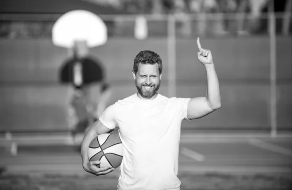 Feliz hombre muscular deportista baloncesto jugador levantado dedo celebrar pelota al aire libre, deporte — Foto de Stock