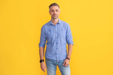 Sarı arka planda el saati olan gülümseyen yetişkin adam, moda aksesuarı.