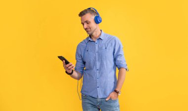 Gülümseyen olgun bir adam kulaklıkla müzik dinler ve telefonla konuşur, iletişim kurar.