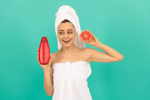 Gelukkig vrouw in handdoek met grapefruit shampoo fles op blauwe achtergrond — Stockfoto
