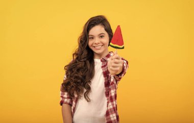 Uzun kıvırcık saçlı mutlu çocuk sarı arka planda lolipop karamel şekeri ve diş bakımı gösteriyor..