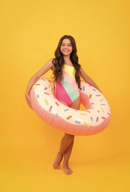 Sarı arka planda donut şişirilebilir yüzüklü mayolu mutlu genç kız, yaz zamanı..