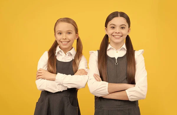 Niños felices usan uniforme escolar manteniendo los brazos cruzados fondo amarillo, 1 de septiembre —  Fotos de Stock