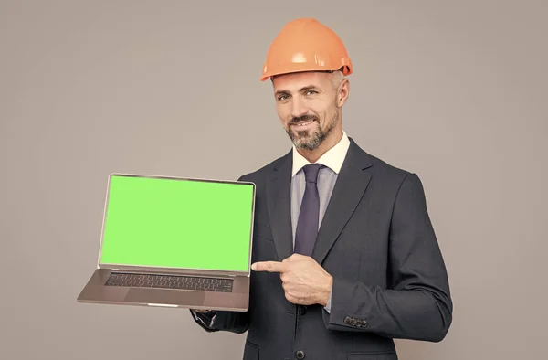 Glad man i hård hatt pekar finger på bärbar grön skärm för kopiering utrymme, presentera produkten. — Stockfoto