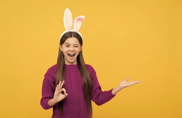 Bambino adolescente in orecchie di coniglio pasquale che presenta il prodotto e mostra gesto ok, spazio copia, vacanza pasquale. — Foto Stock